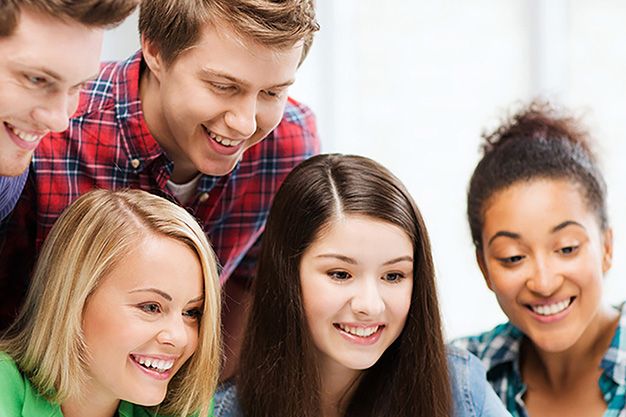 Teenagers gathered around a computer enjoying sharing something